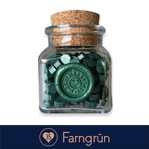 May include: A glass jar filled with green sealing wax pellets. The jar has a cork lid and a label that says "Siegelwerkstatt".