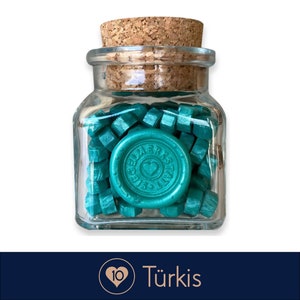 May include: A glass jar filled with teal wax sealing beads. The jar has a cork lid and a teal wax seal with the text "Siegelwerkstatt" and a heart.