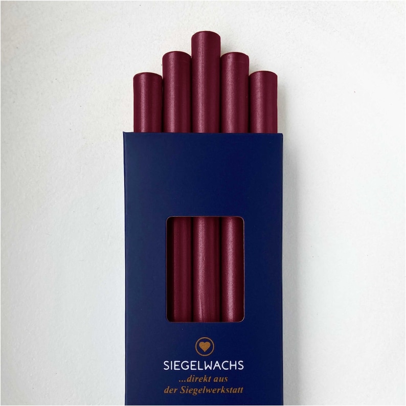 Puede incluir: Una caja de seis barras de cera de sellado color burdeos. La caja es azul con letras doradas que dicen "SIEGELWACHS...direkt aus der Siegelwerkstatt".