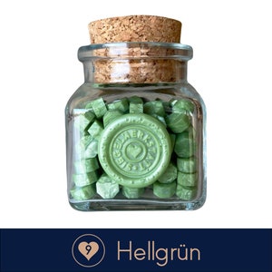 May include: A glass jar filled with green sealing wax pellets. The jar has a cork lid and a label that says "Ein Werksatt Siegel".