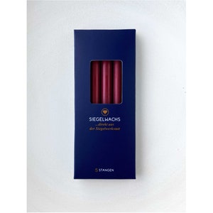 Puede incluir: Una caja de cinco barras de cera para sellar de color burdeos oscuro. La caja es azul marino con letras doradas que dicen "Siegelwachs...direkt aus der Siegelwerkstatt" y "5 Stangen".