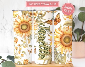 May include: Three stainless steel tumblers with a white background and a sunflower and butterfly design. The middle tumbler has the name "Janelle" written in green cursive.