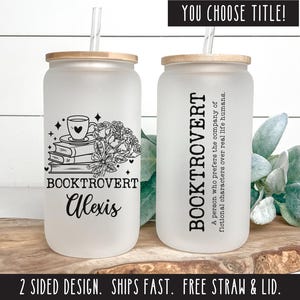 May include: White frosted tumbler with a black and white design of a stack of books, a cup of coffee, and flowers. The text "Booktrovert Alexis" is printed on the tumbler.