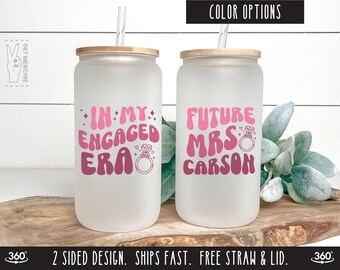 May include: Two frosted glass tumblers with lids and straws. The tumbler on the left says "In My Engaged Era" with a pink ring design. The tumbler on the right says "Future Mrs. Carson" with a pink ring design.