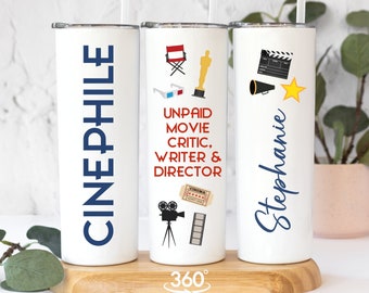 May include: Three white stainless steel tumblers with blue text and movie-themed graphics. The tumblers are on a wooden surface. The text on the tumblers reads "Cinephile", "Unpaid Movie Critic, Writer & Director", and "Stephanie".