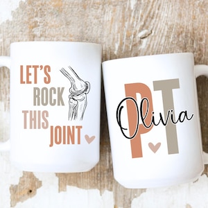 May include: Two white ceramic mugs. One mug has the text "LET'S ROCK THIS JOINT" with a knee joint illustration. The other mug has "PT Olivia" printed on it. Both mugs have a heart symbol.