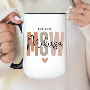 May include: White ceramic mug with a black handle and rim. The mug features the text "EST. 2025" above the name "Melissa" in a script font, with "MSW" in block letters. A small heart graphic is below the name.