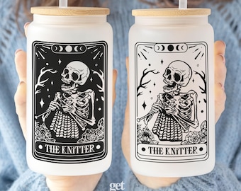 May include: Two frosted glass tumblers with bamboo lids and clear straws. Each features a black graphic of a skeleton knitting, surrounded by floral elements and moon phases, with the text THE KNITTER printed at the bottom of the design.