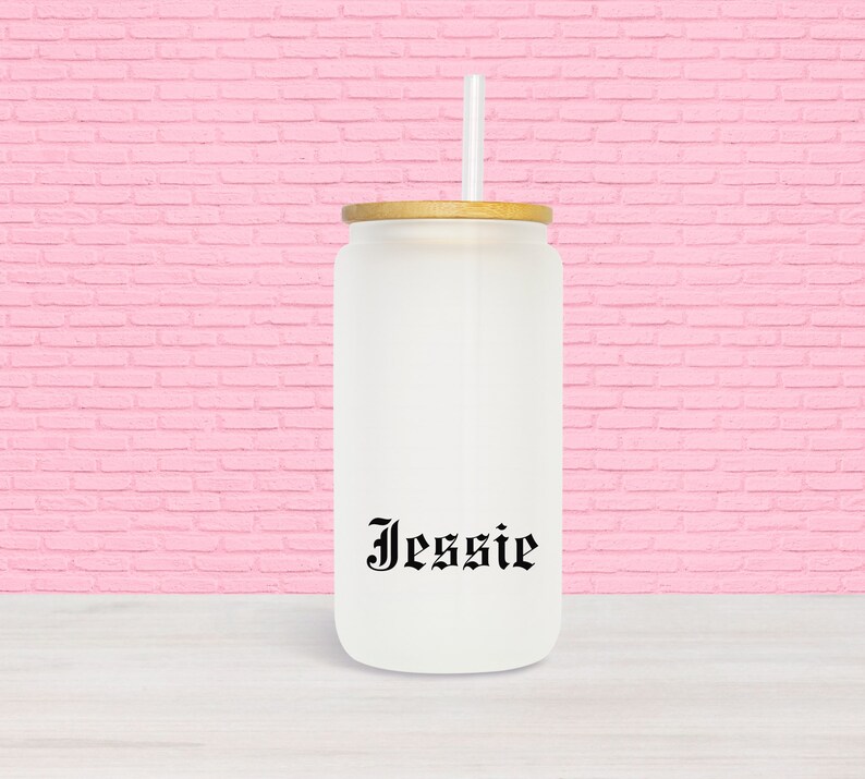 Puede incluir: Un vaso de vidrio esmerilado blanco con tapa de bamb&uacute; y una pajita negra. El vaso tiene el nombre "Jessie" impreso en la parte delantera en una fuente g&oacute;tica negra.