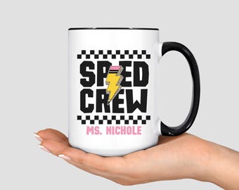 May include: A white ceramic mug with a black handle and rim. The mug features the words "SPEED CREW" in black block letters, a yellow lightning bolt with a pink pencil, and the name "MS. NICHOLE" in pink.
