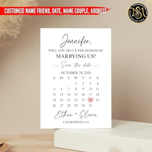 May include: A white wedding invitation card with black script. The text reads "Jennifer, Will you do us the honor of marrying us? Save the date." The date is October 24, 2026, with the names Ethan and Olivia.