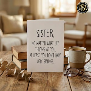 May include: A greeting card with the text "SISTER, NO MATTER WHAT LIFE THROWS AT YOU, AT LEAST YOU DON'T HAVE UGLY SIBLINGS." is displayed on a wooden table. A coffee mug, books, and eyeglasses are also on the table.