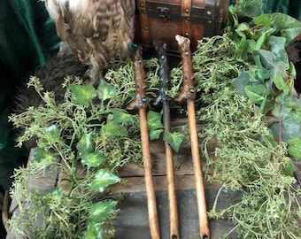 Könnte beinhalten: Drei Holzstäbe mit dunkelbraunen Spitzen und grünen Akzenten, die auf einer Holzoberfläche mit grünem Laub liegen. Die Stäbe sind in einer Reihe angeordnet, wobei die Spitzen nach rechts zeigen. Der Text "Elemental Wands" ist am unteren Rand des Bildes sichtbar.