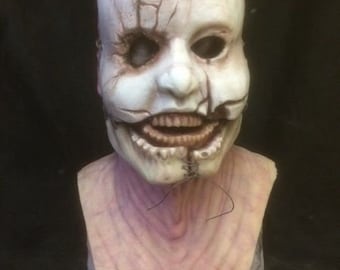 May include: A white latex mask with a cracked and stitched appearance. The mask has a large, open mouth with visible teeth and a single eye.