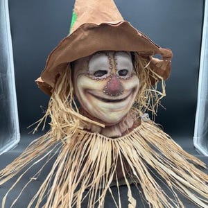 May include: A brown scarecrow mask with a wide-brimmed hat, a stitched-on face, and a straw-like fringe around the neck.