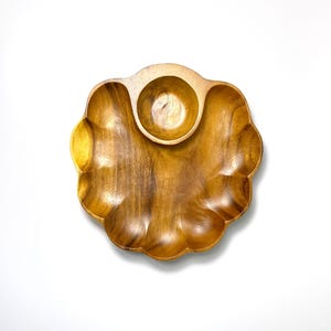 May include: A scalloped wooden serving tray with a natural brown wood grain finish. The tray features a large, curved main section with a smaller, circular bowl integrated into the top center, creating a distinct flower-like shape.