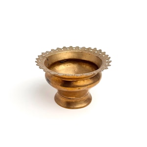 May include: A small, round, metallic gold-toned bowl with a pedestal base. The bowl features a wide, flared rim with a decorative, scalloped, and perforated edge pattern. The surface of the bowl has a smooth, polished finish with visible patina.