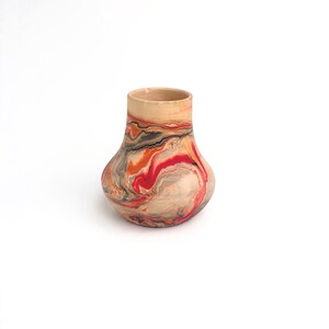 May include: A small, rounded ceramic vase featuring a marbled pattern of vibrant red, orange, black, and cream swirls. The vessel has a narrow neck that flares out into a wider, bulbous body with a smooth, matte finish throughout the exterior.