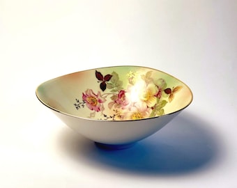 Peut inclure: Un bol en céramique blanche de forme organique irrégulière avec un bord doré. L'intérieur présente un motif floral délicat composé de roses roses et jaunes, de feuilles vertes et d'un feuillage sombre sur un fond vert pâle et doux.