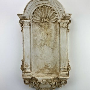 Puede incluir: Un estante de pared decorativo blanco y adornado con un diseño de concha y un acabado desgastado.