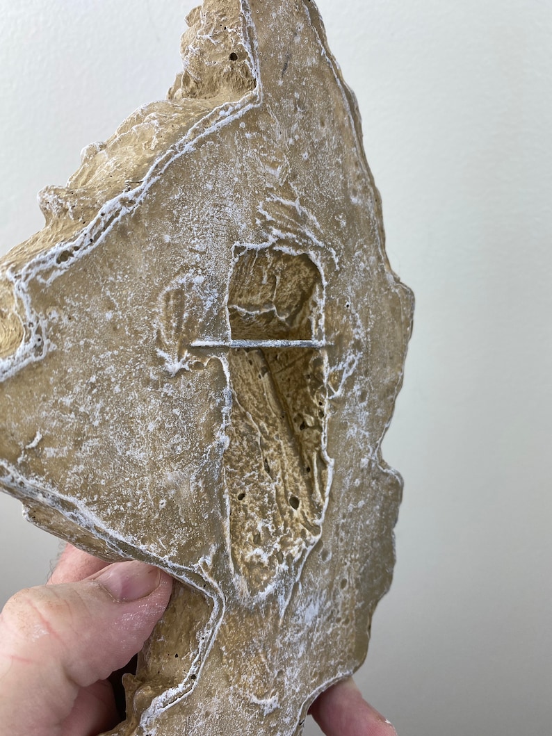 May include: A beige, textured, rock-like object with a hole in the center. The object has a rough, uneven surface and appears to be made of concrete or plaster.