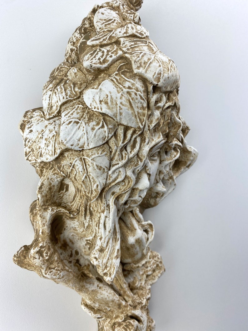 May include: A white ceramic sculpture of a woman's head with leaves and vines covering her hair. The sculpture has a distressed, aged look with brown and white paint.