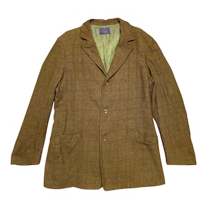 Op de afbeelding: Een bruine tweed blazer met een enkele rij knopen en vier knopen. De blazer heeft twee klepzakken aan de voorkant en een groene voering.