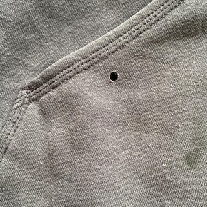 Pode incluir: Close-up de tecido cinza escuro com um buraco vis&iacute;vel. O tecido tem uma apar&ecirc;ncia texturizada e &eacute; costurado ao longo das bordas. A costura &eacute; em um tom de cinza mais claro, criando um contraste.