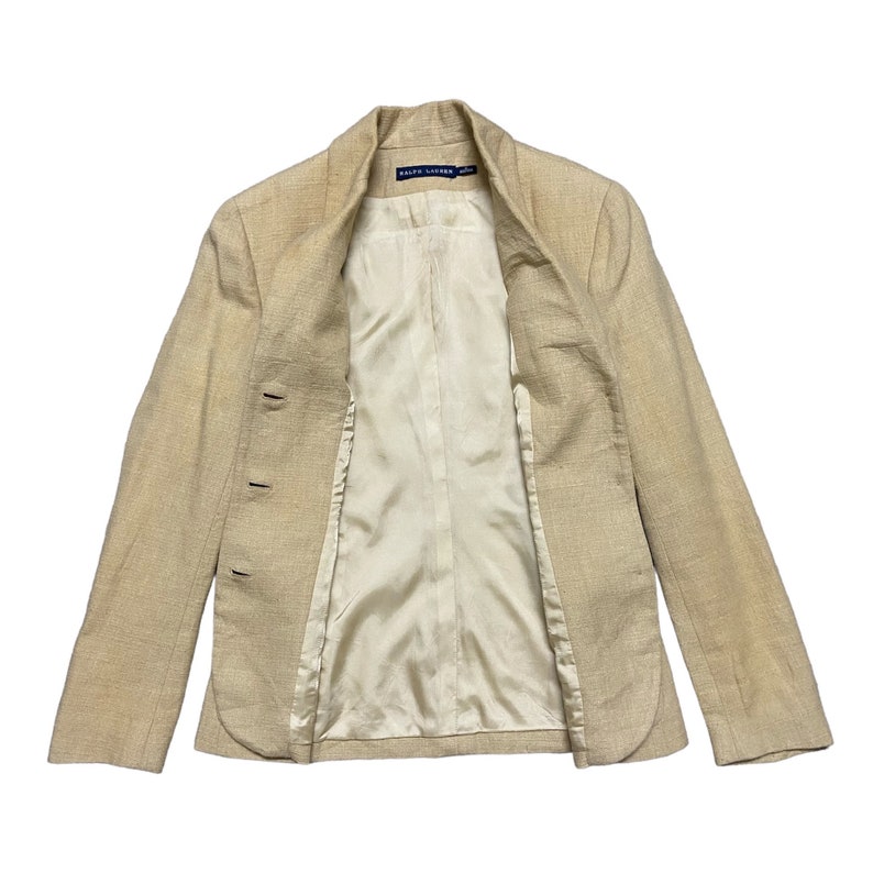 May include: A beige blazer with a  "RALPH LAUREN" label on the inside collar. The blazer has a  double-breasted closure and a  satin lining.