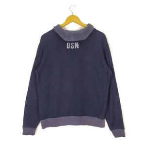 May include: A navy blue sweatshirt with a ribbed collar and cuffs. The sweatshirt has a white "USN" logo on the back.