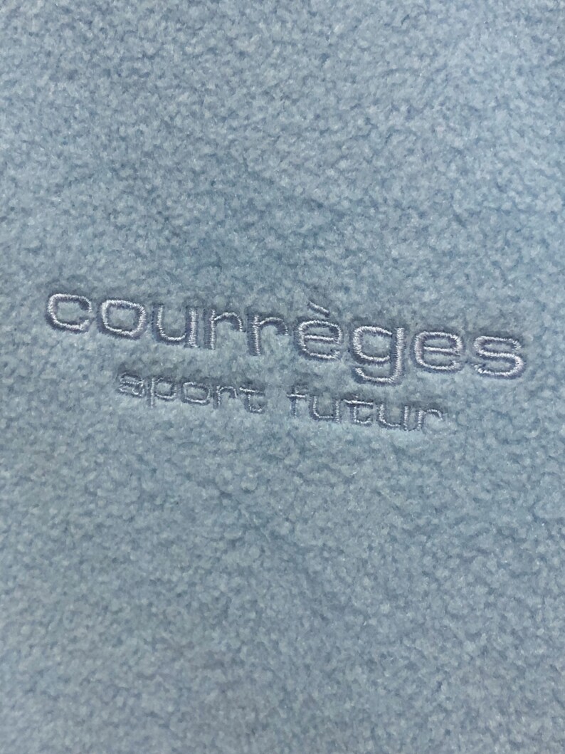 May include: A light blue fleece jacket with the embroidered text "Courr&egrave;ges sport futur" in white.