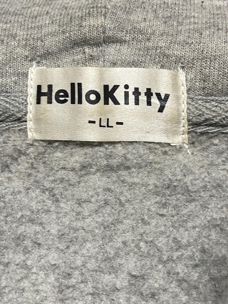 May include: A white tag with black text that reads "Hello Kitty" and "LL" on a grey sweatshirt.