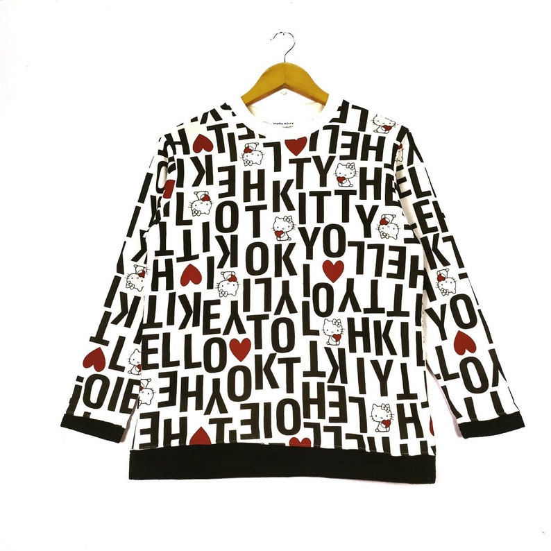 May include: White long-sleeved sweatshirt with an all-over print of Hello Kitty, hearts, and the words "I Love Kitty" in black and red.