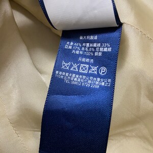 May include: Blue fabric care label with text in Japanese and English. The label states the fabric composition is 44% silk, 33% linen, 17% wool, 6% nylon, and 100% copper for the lining. The label also states "Made in Italy" and provides instructions for dry cleaning only.