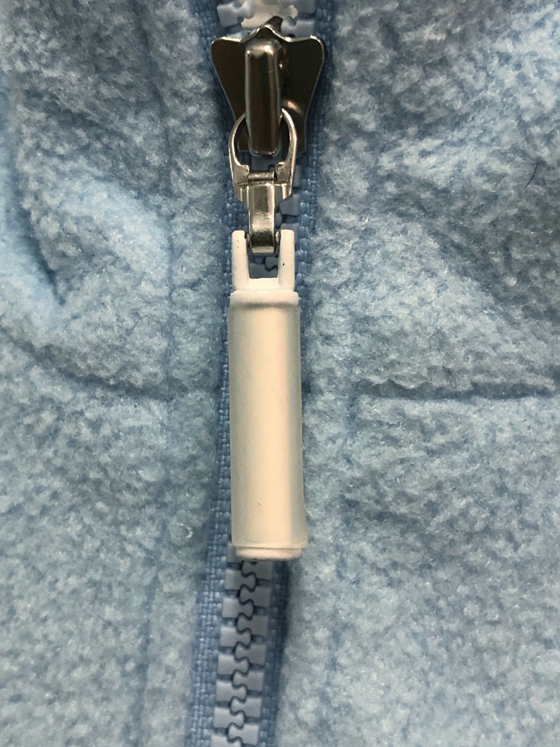 May include: A close-up of a light blue zipper with a white pull tab. The zipper is partially closed.