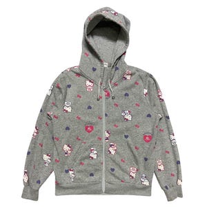 May include: A grey zip-up hoodie with a Hello Kitty print. The hoodie features a pink Hello Kitty with a red heart and the text "Hello Kitty 40th Anniversary" in a pink circle. The hoodie is covered in a pattern of Hello Kitty characters, hearts and bows.