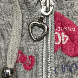 May include: A grey zip-up hoodie with a heart-shaped zipper pull. The hoodie has a pink heart with the text "40 ANNIVERSARY" printed on it.