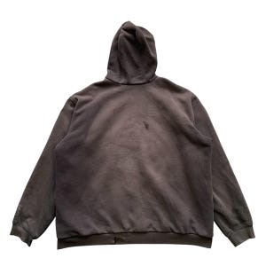 Pode incluir: Um moletom marrom escuro com capuz e mangas compridas. A vista traseira revela um design simples e casual. O tecido parece macio e desgastado.