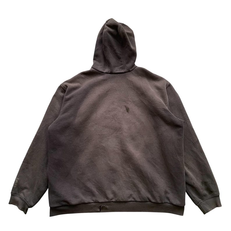 Pode incluir: Um moletom marrom escuro com capuz e mangas compridas. A vista traseira revela um design simples e casual. O tecido parece macio e desgastado.