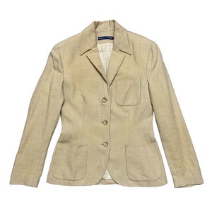 May include: A beige linen blazer with a single breasted closure and four buttons. The blazer has two front pockets and a single chest pocket. The label reads "Ralph Lauren".