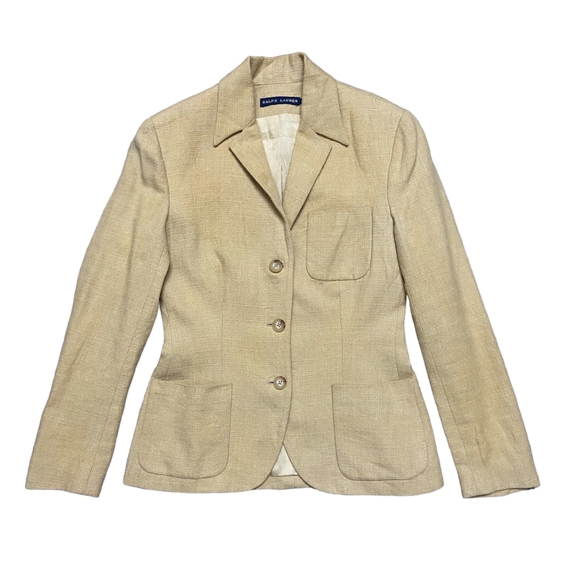 May include: A beige linen blazer with a single breasted closure and four buttons. The blazer has two front pockets and a single chest pocket. The label reads "Ralph Lauren".