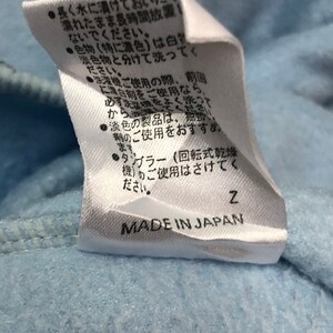 May include: White care tag with black text on a light blue background. The tag contains instructions for washing and drying the garment. The text reads: "Long soaking or leaving wet for long periods is not recommended.  Wash dark colors (especially dark colors) separately from light colors.  When using a washing machine, turn the garment inside out.  When using a dryer, use a low heat setting.  Do not use a dryer.  Made in Japan."