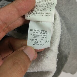 May include: A white tag with black text and symbols. The tag says "90% COTONE - COTTON COTON - BAUMWOLLE 10% VISCOSA - VISCOSE VISCOSE - VISKOSE MADE IN ITALY". The tag has a 40 degree Celsius washing symbol, a do not bleach symbol, a low iron symbol, and a do not dry clean symbol.