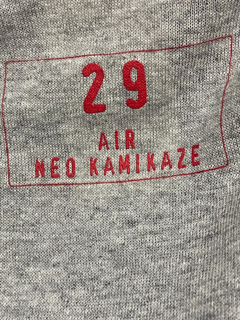 May include: A gray t-shirt with a red rectangular patch that says "29 AIR NEO KAMIKAZE" in white letters.