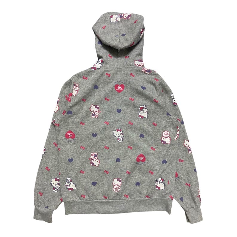 May include: A grey hooded sweatshirt with a Hello Kitty print. The sweatshirt features a repeating pattern of Hello Kitty characters, hearts, and bows. The text "Hello Kitty 40th Anniversary" is printed on the front of the sweatshirt.