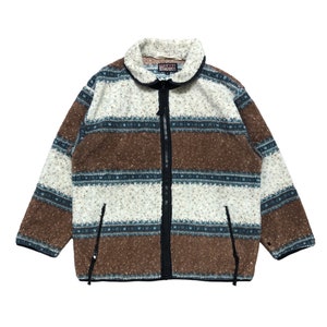 Pode incluir: Uma jaqueta de fleece listrada em marrom, branco e azul com fecho de zíper. A jaqueta tem um colar alto e dois bolsos com zíper. O nome da marca "FLASH" é visível no zíper.