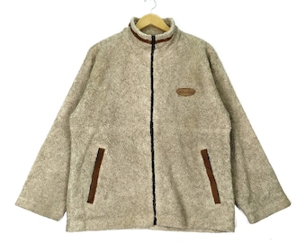 May include: A beige fleece jacket with a brown zipper and brown trim. The jacket has a brown leather patch with the word "Whistle" on it.