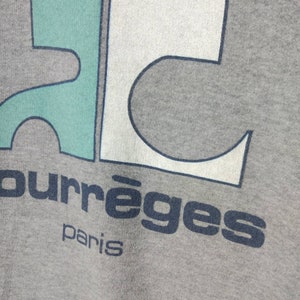 May include: A gray sweatshirt with a blue, white, and green graphic design. The text "Courr&egrave;ges Paris" is printed below the graphic.