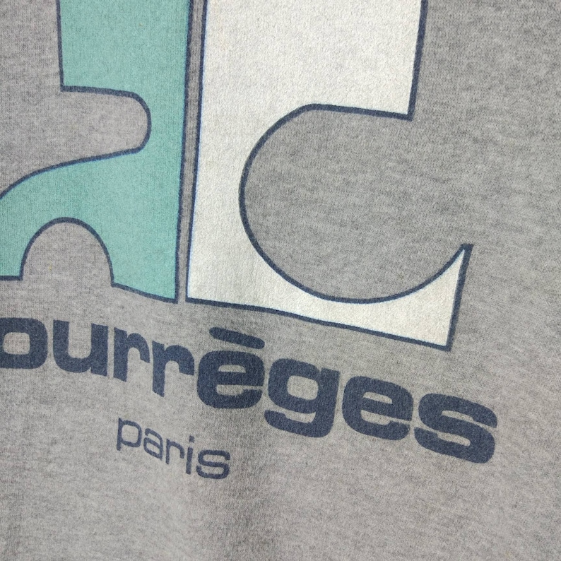 May include: A gray sweatshirt with a blue, white, and green graphic design. The text "Courr&egrave;ges Paris" is printed below the graphic.