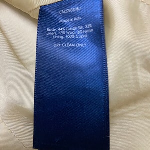 May include: A blue fabric label with white text that reads "07622835HB", "Made in Italy", "Body: 44% Tussan Silk, 33% Linen, 17% Wool, 6% Nylon", "Lining: 100% Cupro", and "DRY CLEAN ONLY".